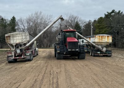 Tractor in a field with two grain carts, one on each side, displaying loading augers extended towards the center. Overcast sky in the background.