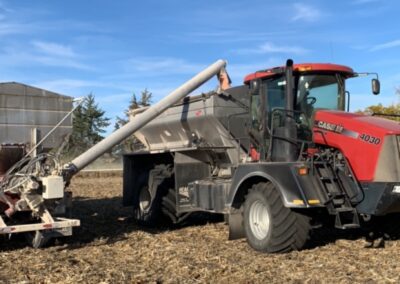 A red Case IH 4030 tractor is positioned in a field with a blue sky overhead. The tractor is connected to a piece of equipment for transporting material, showing a worker actively engaged in the operation amidst harvested crop residue. This image highlights modern agricultural practices and the machinery used in farming.